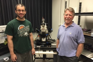 Robert Green (dcha.), y Alex Sonneborn, estudiante de posgrado, junto a Zeiss Axoskop2, un equipo de estimulación optogenética y grabación electrofisiológica que les permite manipular y monitorizar neuronas vivas. Fuente: UT Southwestern.