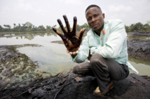 Eric Dooh, en el pueblo de Goi, Ogoniland, mostrando la contaminación del mar por el petróleo debido a una actividad de la empresa Shell en Nigeria. Fuente: "Marten van Dijl/Friends of the Earth Netherlands