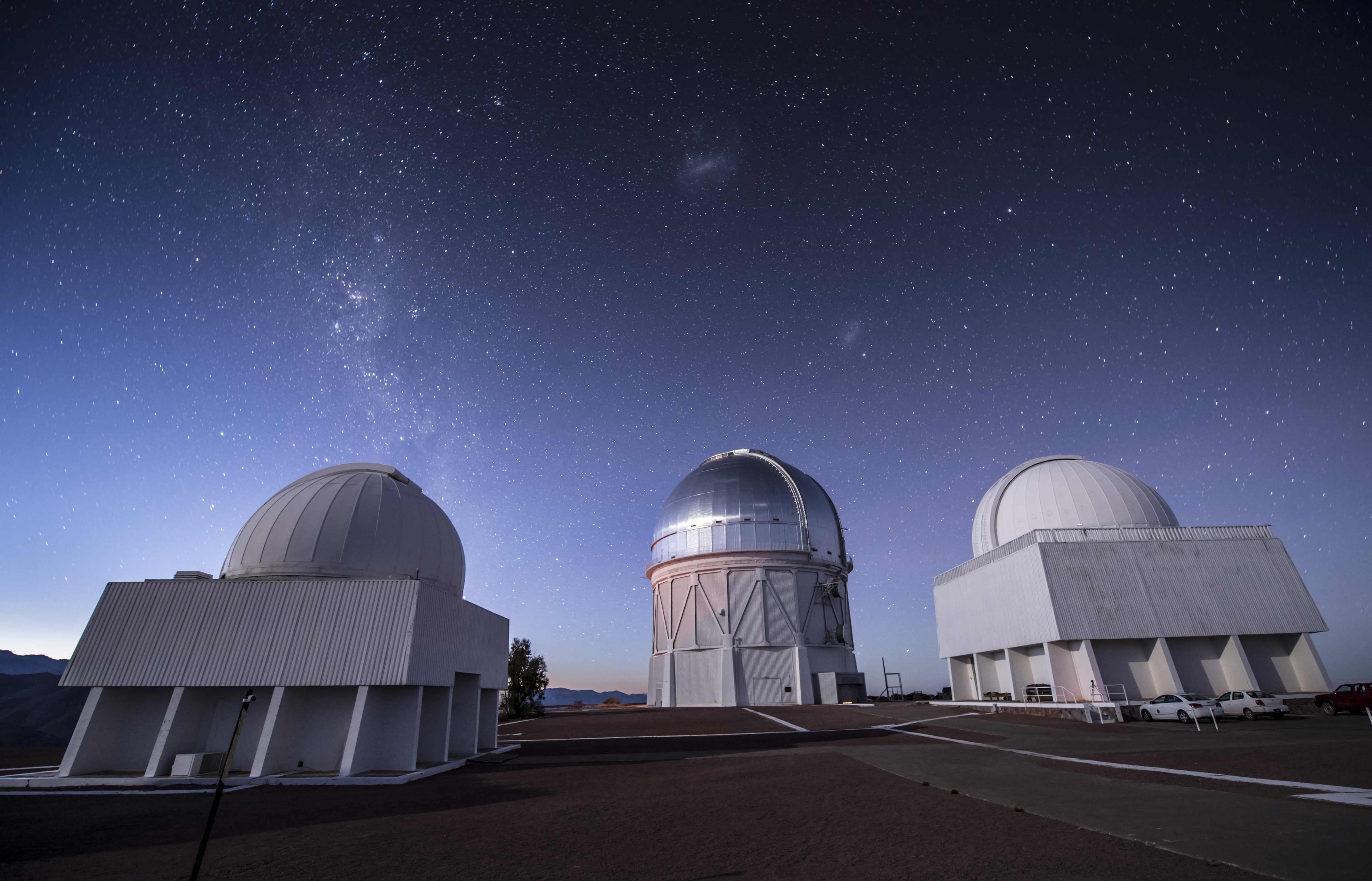 Vista del telescopio Blanco, situado en el observatrio de Cerro Tololo, en los andes chilenos. El telescopio se encuentra bajo la cúpula metálica del centro de la imagen. Sobre dicha cúpula son visibles las nubes de Magallanes, dos galaxias enanas, satélites de la Vía Láctea. Crédito de la imagen: DES Collaboration y Fermilab.