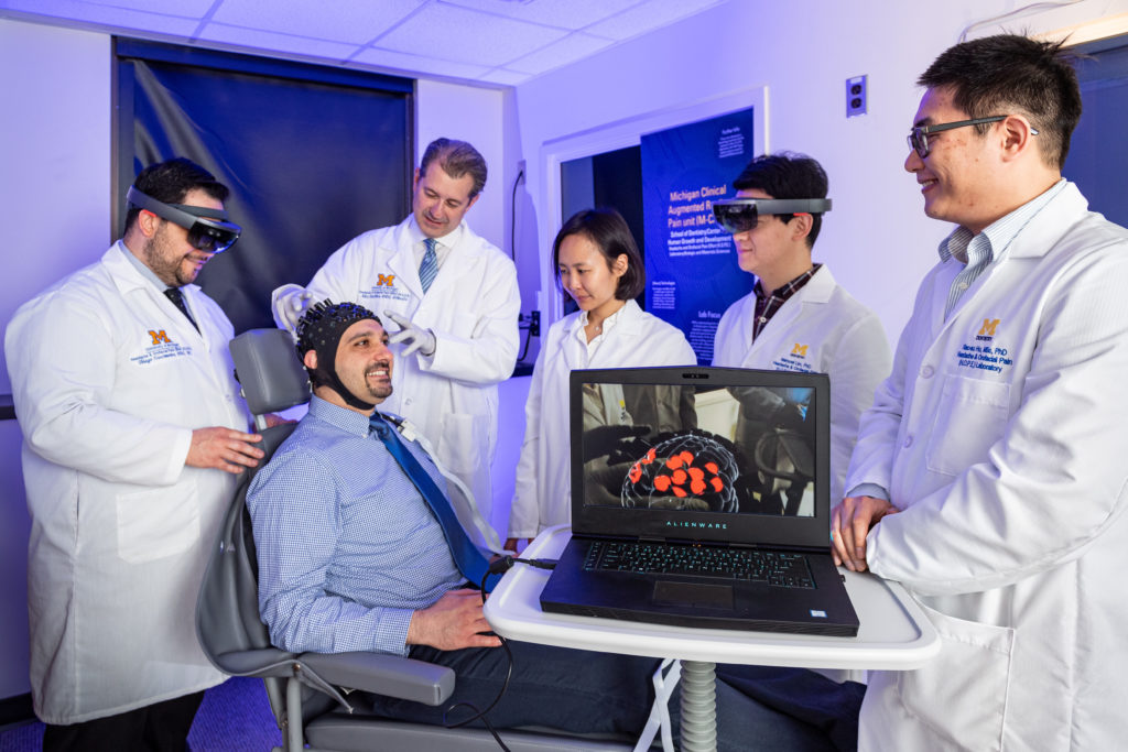 Thiago Nascimento, a la izquierda, ve la actividad cerebral en tiempo real de un paciente mientras usa gafas de realidad aumentada. La imagen del ordenador muestra la firma del dolor en el cerebro. De izquierda a derecha, también en la foto, Alex DaSilva, Dajung Kim, Manyoel Lim y Xiao-su Hu, los protagonistas de este desarrollo. Foto: Universidad de Michigan.