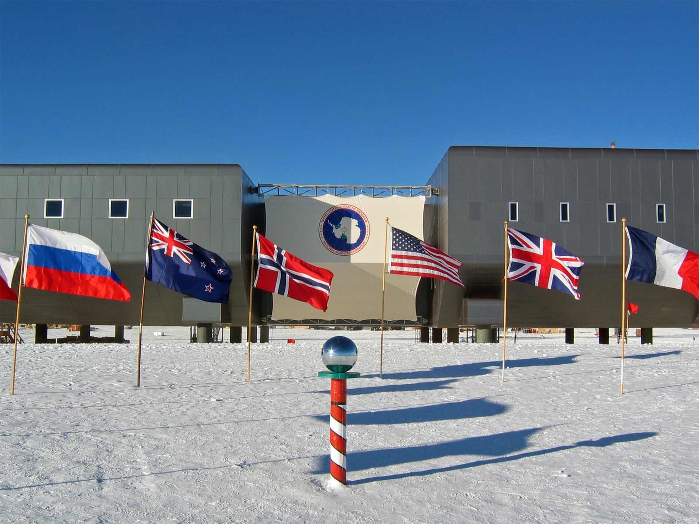 Banderas de los firmantes del Tratado Antártico en la Base Amundsen-Scott y la señal que indica el llamado Polo Sur Geográfico Ceremonial. Foto: Bill Spindler, U.S. Antarctic Program, National Science Foundation.